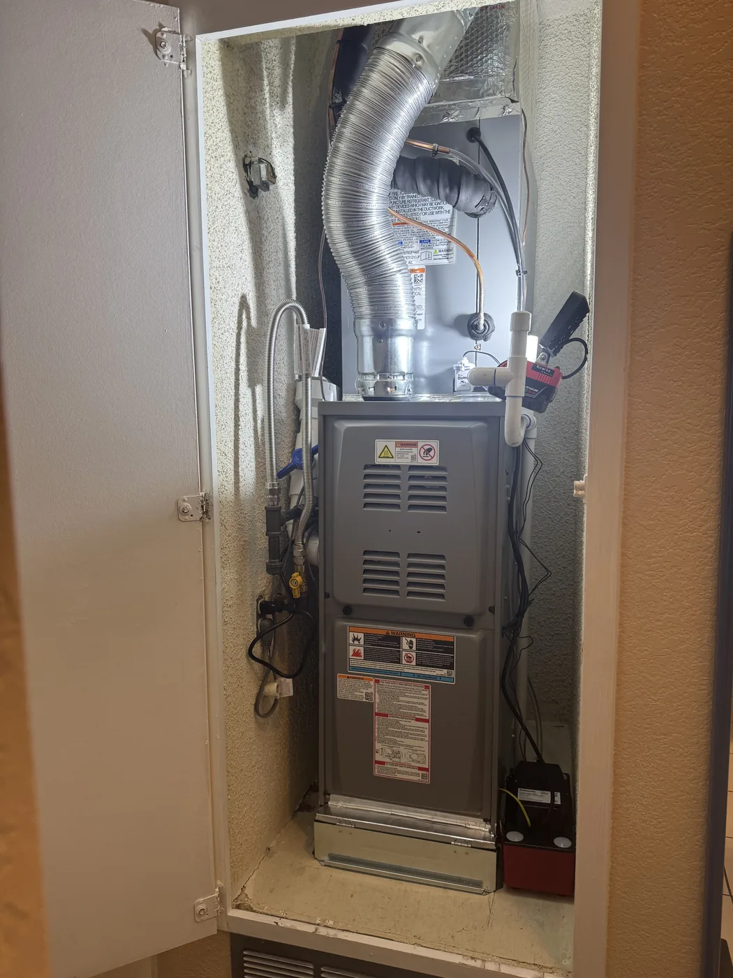 New furnace set in a hallway closet with flexible ducting connected above it