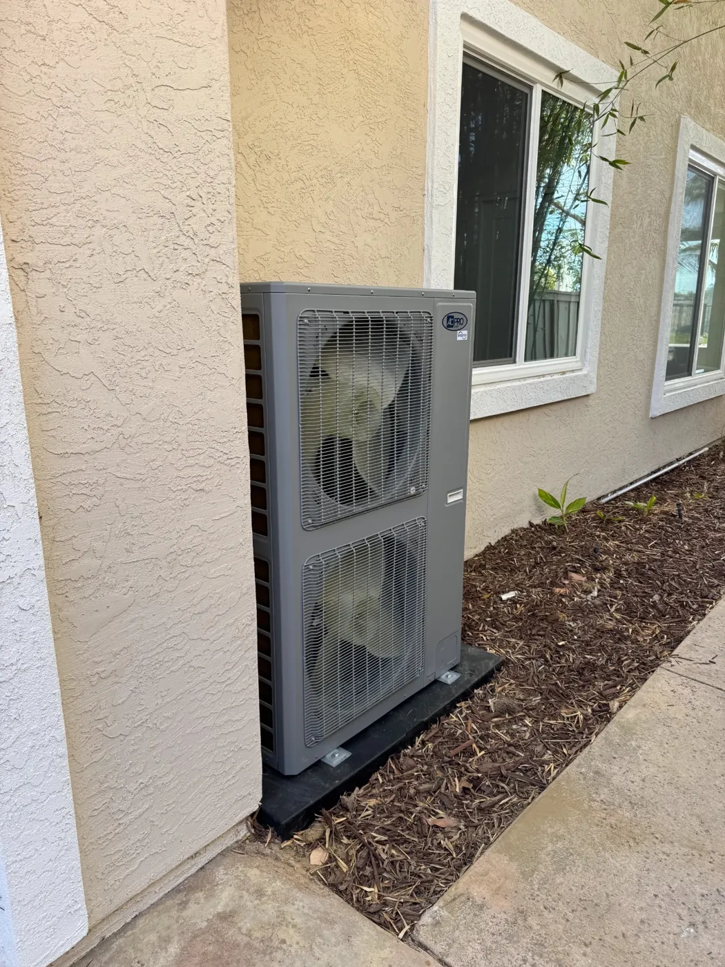 New dual fan side discharge AC condenser installed against a stucco San Diego home